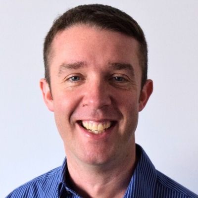 Headshot of a man wearing a dark blue shirt smiling at camera.